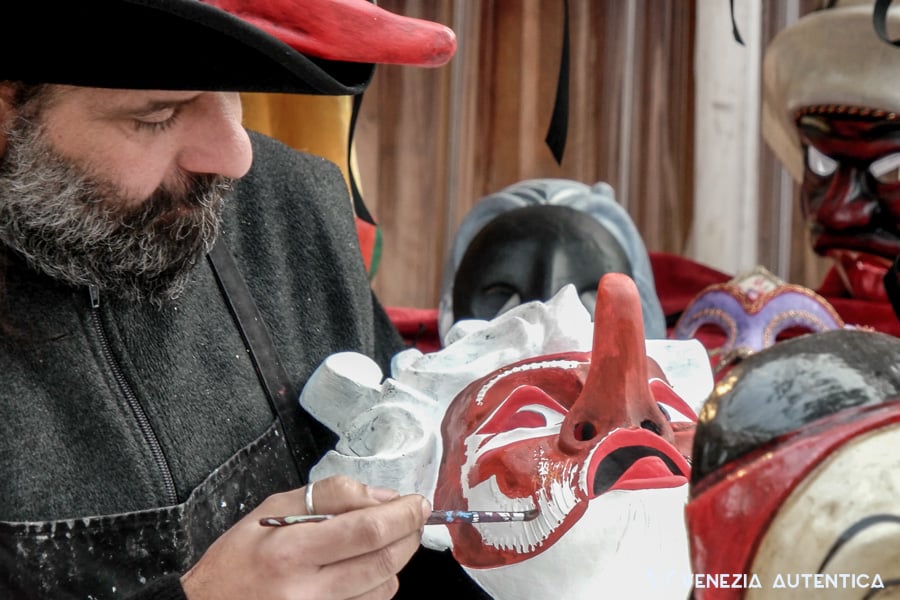 mascarer, or glass maker, colouring in red the mask he is holding. On the background, out of focus, a few masks can be seen.
